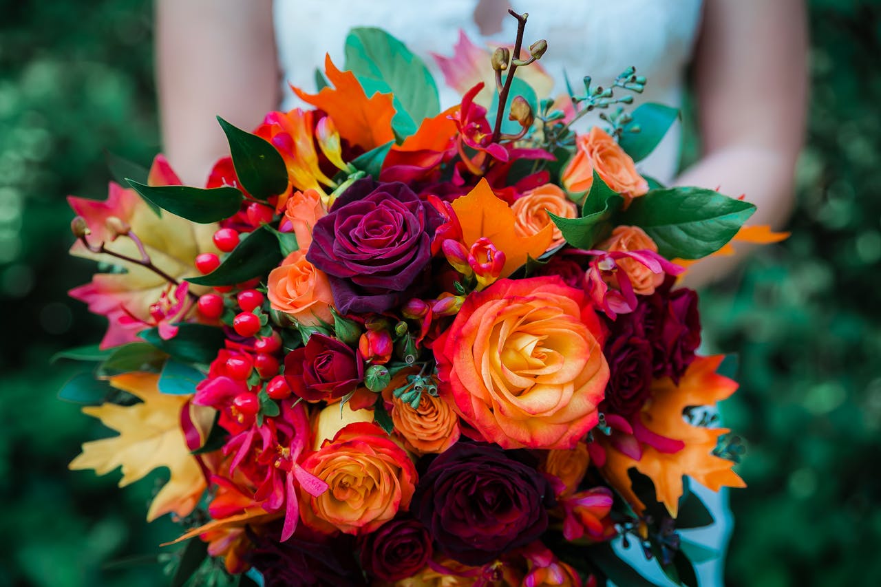 A colorful fall-themed wedding bouquet featuring roses and autumn leaves, perfect for a vibrant wedding.